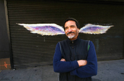 Unidentified man posing with arms crossed in front of a mural depicting angel wings