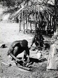 While his young assistant is using a bellows to keep the fire, a Batenga blacksmith is forging a spear-head