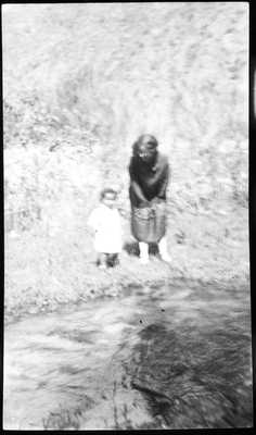 Unidentified woman and child standing on river bank