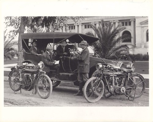 Motorcycle Policemen Archie Cooper and Leslie Cooper Pretending to Write Traffic Ticket in Front of Library