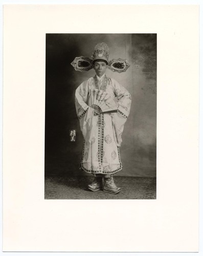 Actor in the role of high court official wearing a headdress and holding a fan /
