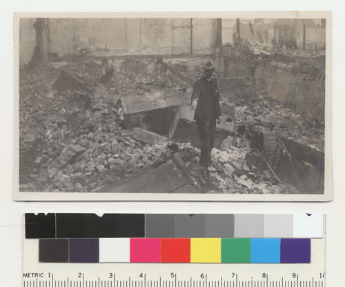 Leo directing movements. [Man standing among ruins with safes, unidentified location.]