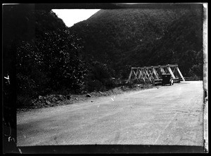 Early-model automobile near a wooden trestle bridge in the mountains