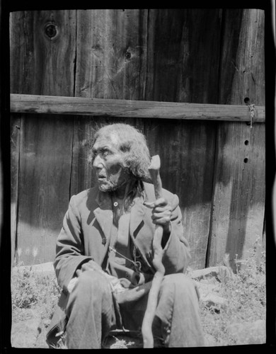 Native American man in front of a wooden plank house