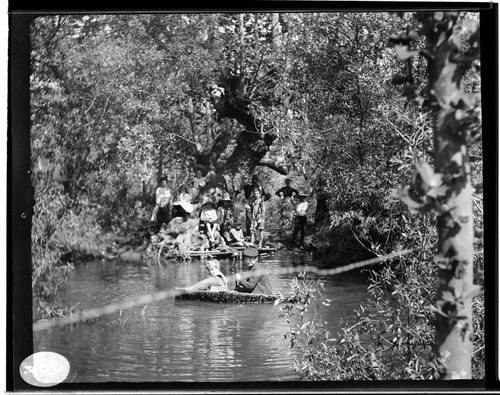 Boys and girls in a boat and on the shore at a pond