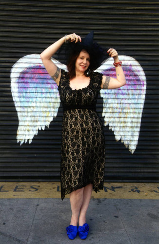 Unidentified woman with witch's hat posing in front of a mural depicting angel wings