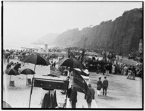 A beach scene, showing a crowd of people with umbrellas on a sandy beach