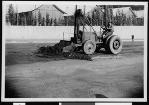 Man using a tractor to load (and remove?) the old surface during the resurfacing of an unidentified street