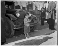 Young boy stands barefoot in front of a car in the slums, Los Angeles, 1925-1945