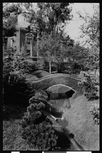 Arched bridge over water in the sunken gardens of Exposition Park, ca.1925