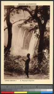 Man carrying a pole walks before a waterfall, Congo, ca.1920-1940