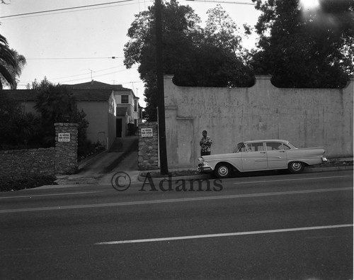 Man standing next to wall by houses, Los Angeles, 1964