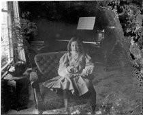 Girl seated on upholstered chair near piano, c. 1912