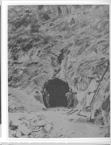 Two men standing at the mouth of the tunnel set in a rocky mountain on the Kern River #1 Hydro Plant development