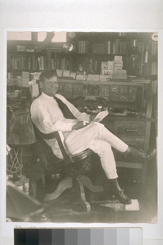 [Jack London sitting on chair next to a desk.]