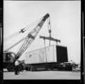Crane lifting and transferring a large trailer crate between a railroad flatcar and a flatbed truck