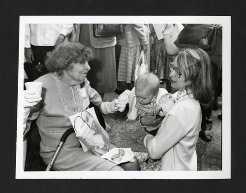 A young woman holds her baby while her fellow Scripps alum shakes the baby's hand, Scripps College