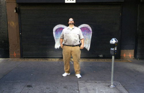 Unidentified man in sunglasses posing in front of a mural depicting angel wings