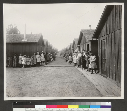 [Unidentified refugee camp. Children posing along rows of cottages.]