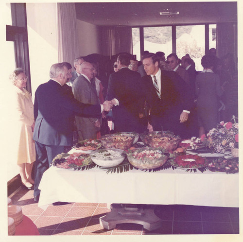 Buffet Table: President Banowsky shaking hands with a man; Mrs. Dorothy Moore between them