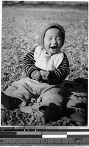 Smiling baby sitting outdoors on a blanket, Japan, ca. 1948