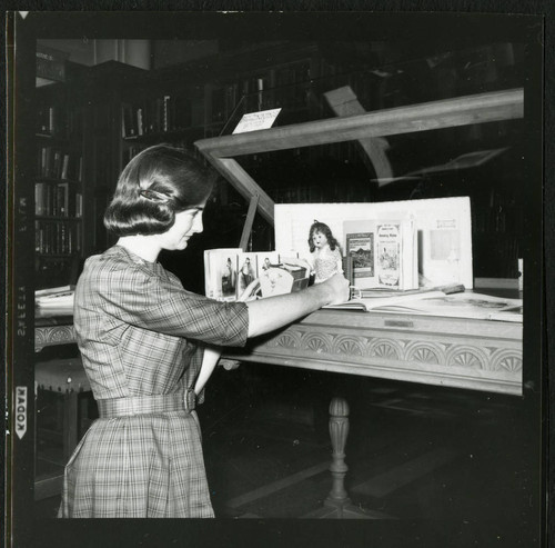 Student librarian arranging a doll in a display case in Denison Library, Scripps College