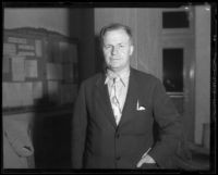 Man in jacket with rumpled collar and tie near bulletin board, [1933-1938?]