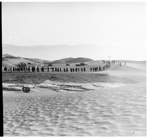 Long line of people walking away from a cross in the desert for a funeral
