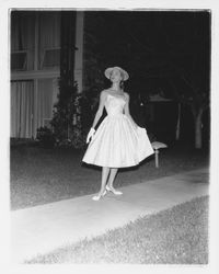 White party dress modeled on walkway in the Flamingo Hotel courtyard at the Sword of Hope fashion show at the Flamingo Hotel, Santa Rosa, California, 1960