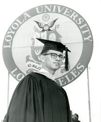 Student at Loyola University commencement in front of university banner, 1969