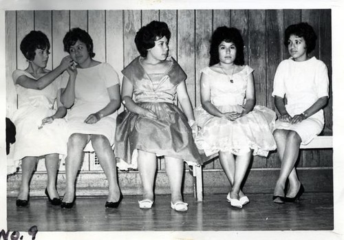 Five teenage girls in dresses sitting along a wall