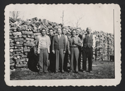 Men in front of large wood pile