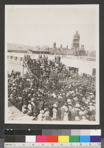 [Crowd gathered at unidentified event. At Van Ness Ave. and Market St. City Hall in distance.]