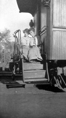 Two women seated on the back steps of a railroad car in Stirling City