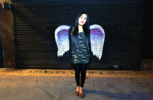 Unidentified woman with long hair posing in front of a mural depicting angel wings