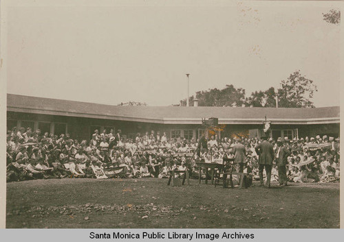 Youth assembly is gathered for a photo with a large format camera in front of the dining hall at Institute Camp, Temescal Canyon, Calif., July 1922