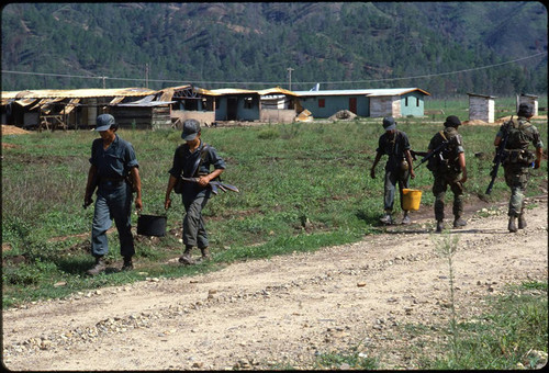 Contras carry containers down a road, Nicaragua, 1983