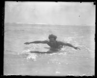Surfer and Olympic swimmer Duke Kahanamoku in the ocean paddling on surfboard in Los Angeles, Calif., circa 1920