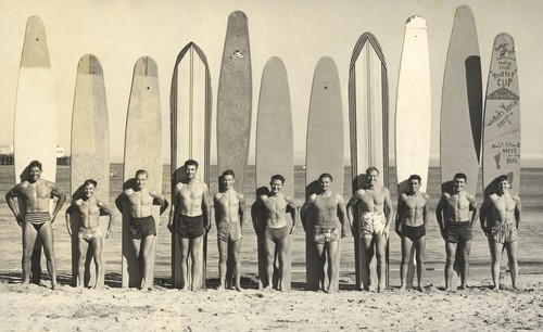 Club surfers standing in front of surfboards: Don Patterson, Harry Murray, Rich Thompson, Alex Hokamp, Blake Turner, Bill Grace, Buster Steward, Fred Hunt, Harry Mayo, Pinky Pedemonte, Tommy Roussel at Cowell Beach