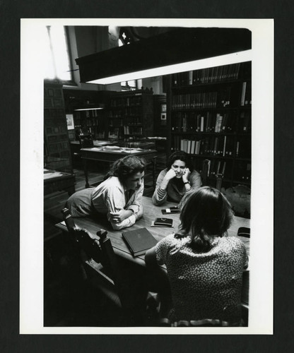 Three Scripps students conversing at a table in Denison Library, Scripps College
