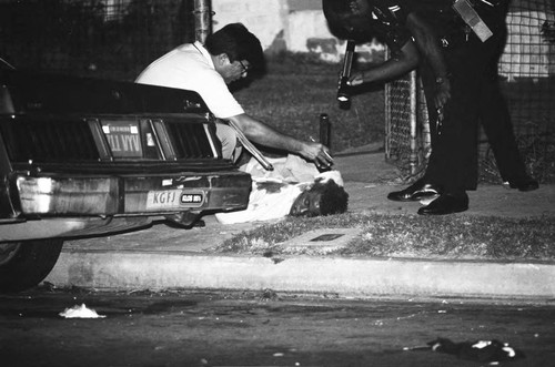 Police examining a body in the front yard of a house on 54th Street, Los Angeles