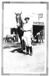 Woman in riding apparel holding reins of horse standing in front of J. N. Vail Riding Academy of Santa Rosa, California, June 1934