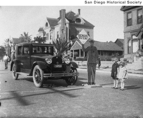 An automobile and two children standing next to a cut-out of a school crossing guard