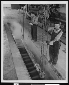 Two unidentified workers lowering chains in a factory, ca.1930