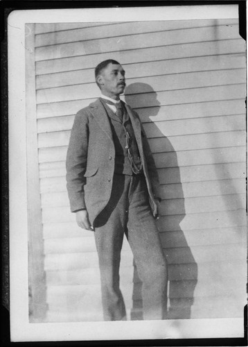 Rev. G. W. Hicks (Cherokee), standing outside house. Rev. Hicks was missionary to the Kiowa tribe for many years. Indian Territory