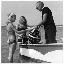 Two unidentified women in swimsuits talk to a man standing in a small boat