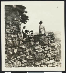Three people peering through a spy-glass at the Glacier Point Lookout in Yosemite National Park, ca.1900