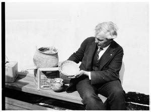 Man seated next to Native American pottery at the Pacific Southwest Museum