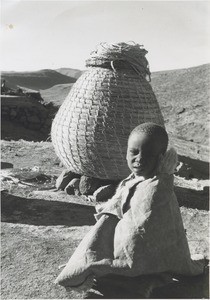 A child in front of a corn storehouse, in mountains near Mohlanapeng