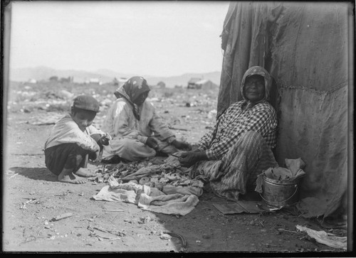 Washoe women and a boy preparing food outside dwelling